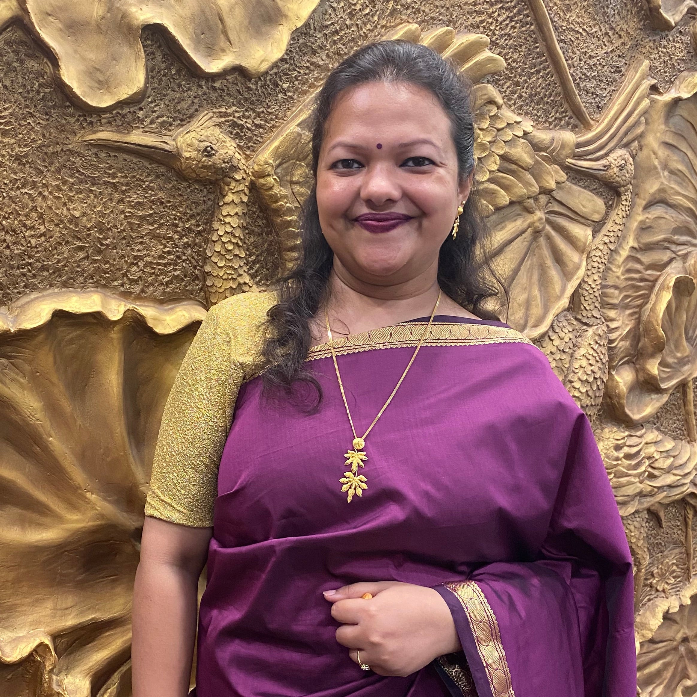 Woman in a purple saree with gold border lying on a textured gold surface